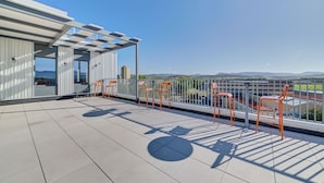 Terraço no telhado com vista para montanhas distantes, um pérgola e várias cadeiras laranja.