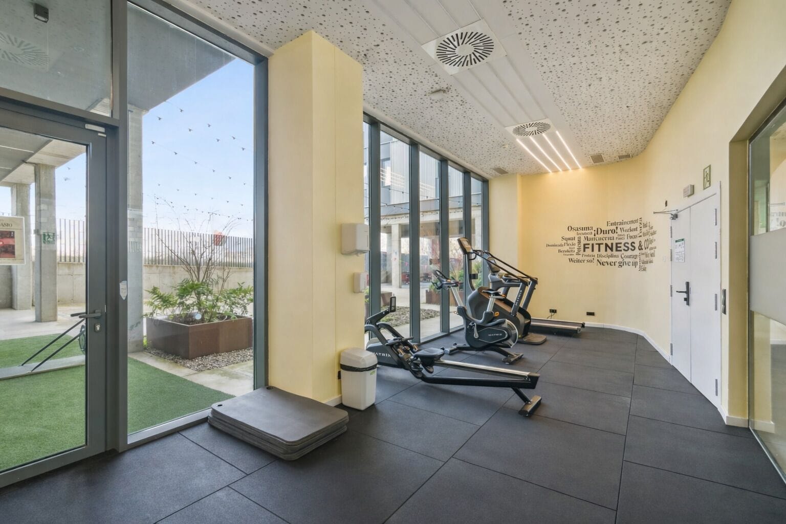Une salle de sport moderne équipée de matériel d’exercice, dotée de grandes fenêtres et agrémentée de décorations murales inspirantes.