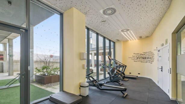 Un gimnasio moderno con equipo de ejercicio, ventanas amplias y arte motivacional en las paredes.