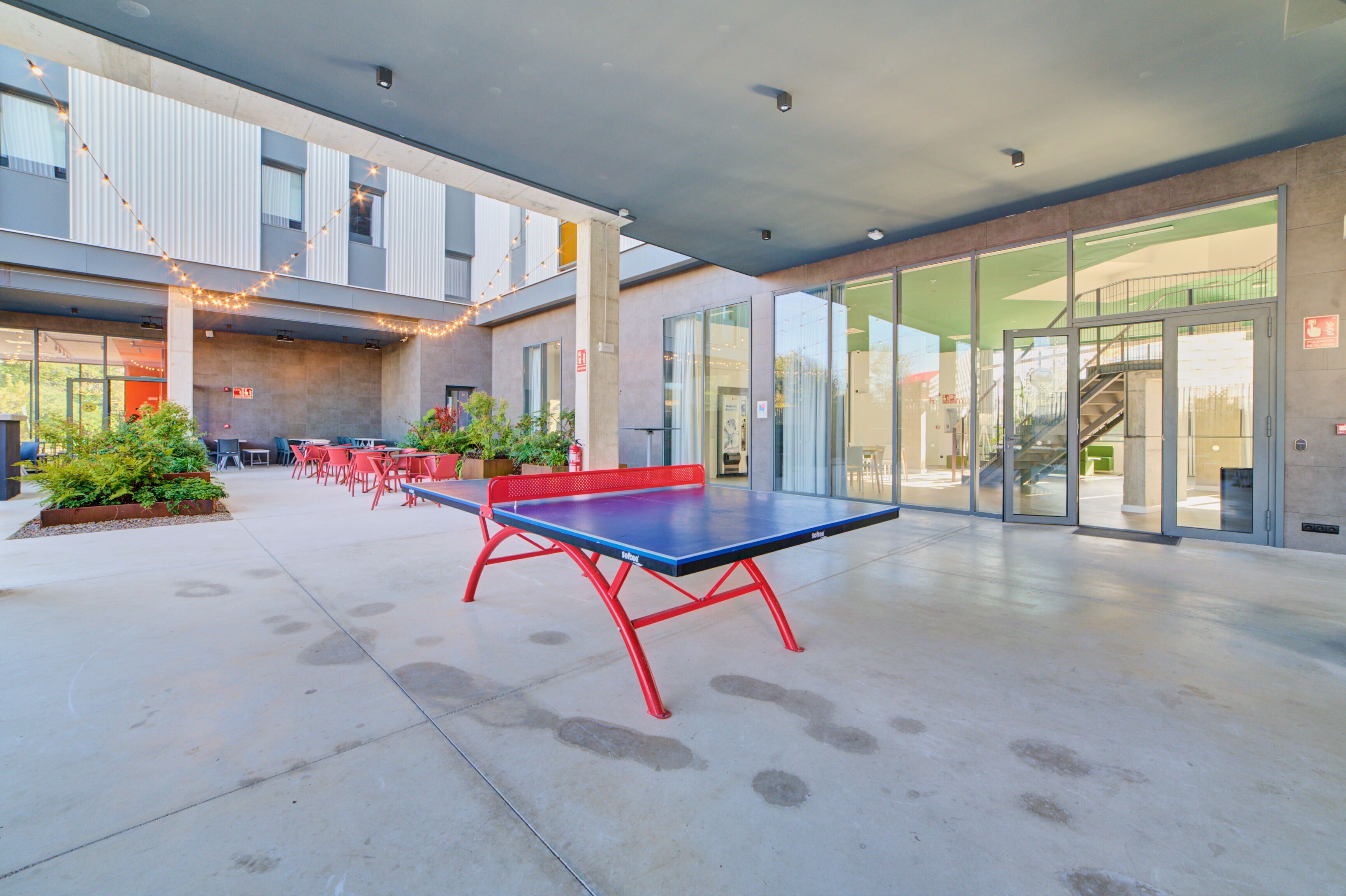 An outdoor seating area with tables and chairs, a ping pong table, and potted plants.