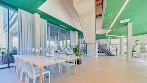 Uma sala de conferência moderna com uma mesa comprida, cadeiras brancas e um vaso de planta.