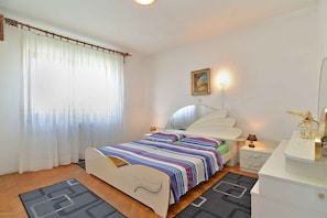 A bedroom with a bed, bedside tables, a nightstand, a lamp, a painting, and a window with curtains.