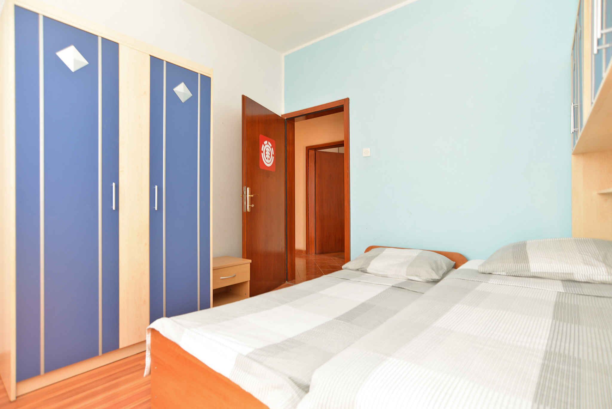 A bedroom with a bed, a wardrobe, a desk, and a door with a fire safety sign.