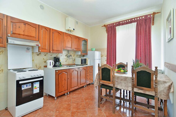A compact kitchen with wooden cabinets, a white stove, a microwave, and a dining area with a table and chairs.
