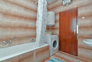 A bathroom with a bathtub, a washing machine, a wooden door, and a sink.