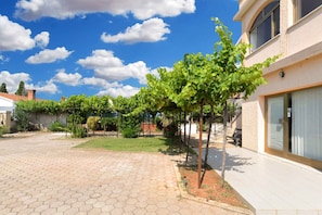 A courtyard with a paved walkway, a small lawn, and a building with a closed shutter.
