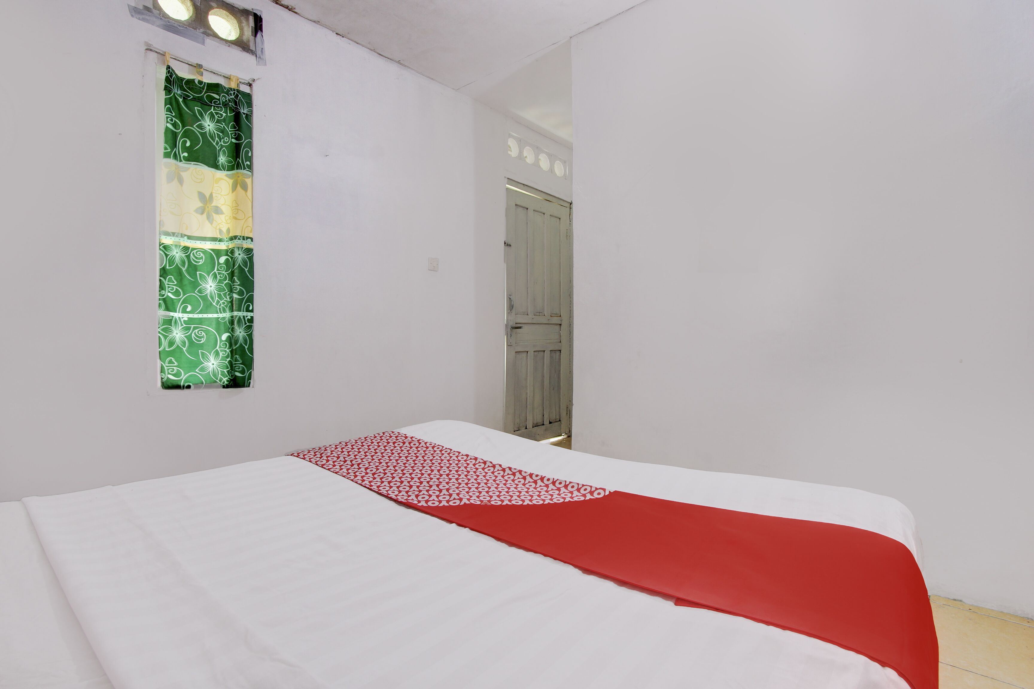 A room with a bed, a window with a green patterned curtain, and a door.