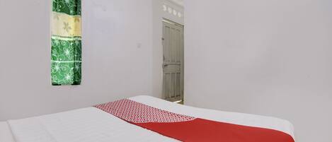 A room with a bed, a window with a green patterned curtain, and a door.