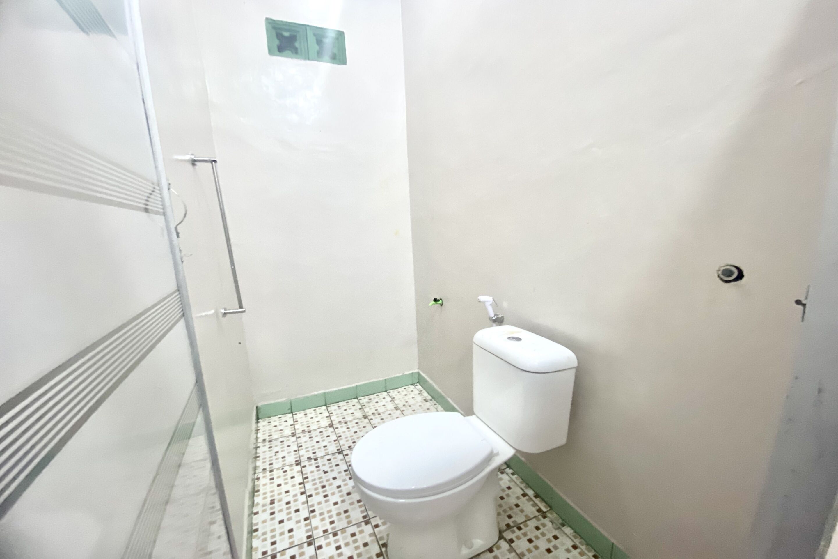 Un baño pequeño y estrecho con inodoro blanco, zona de ducha y suelo de baldosas.
