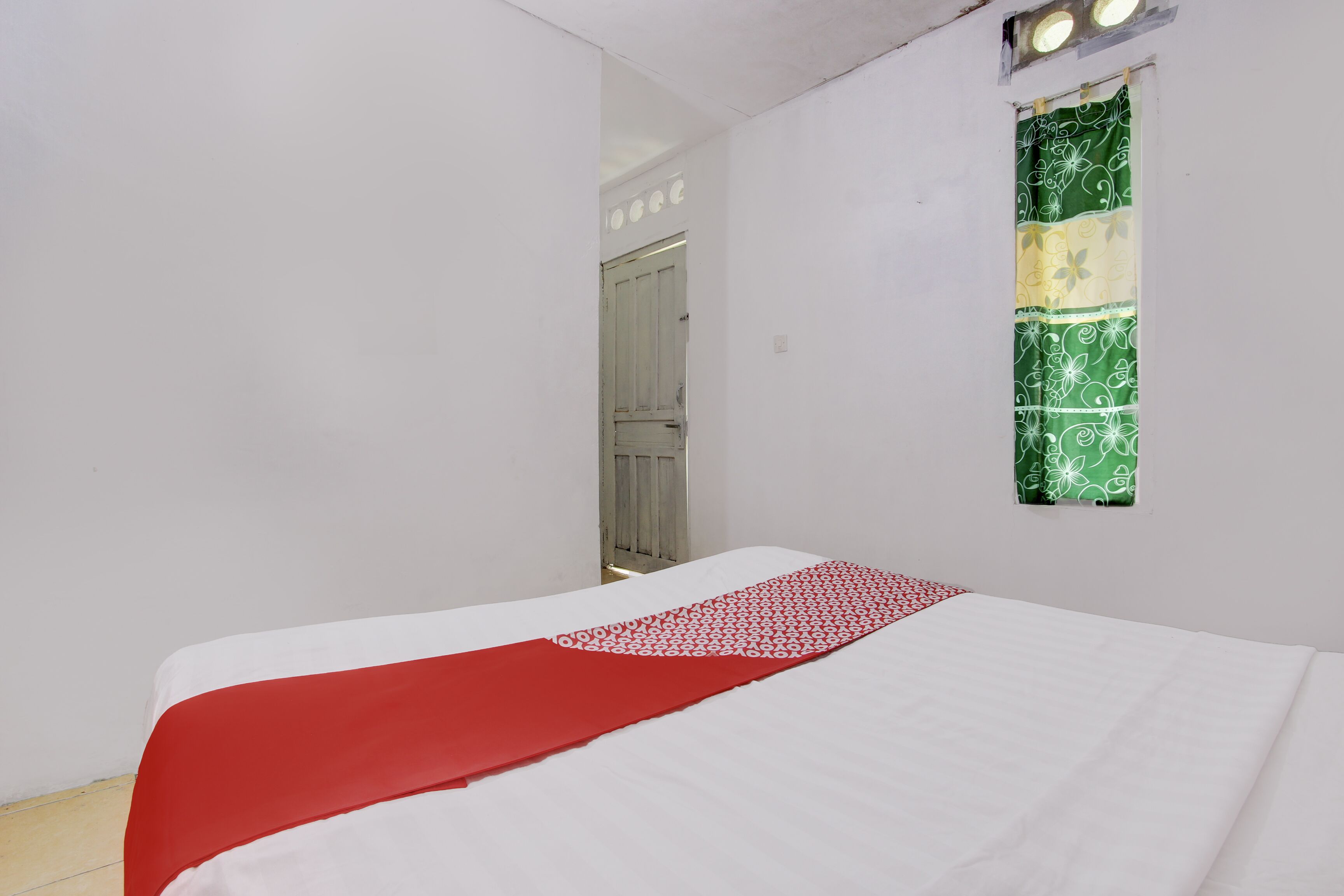 Een kamer met een bed, een raam met een groen en geel gordijn, en een deur op de achtergrond.