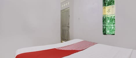 Une pièce avec un lit, une fenêtre ornée d’un rideau vert et jaune, et une porte au fond.