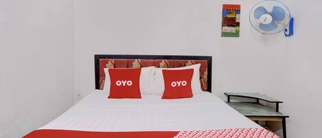 A bed with two pillows labeled "OYO," a small table, a wall-mounted fan, and two posters on the wall.