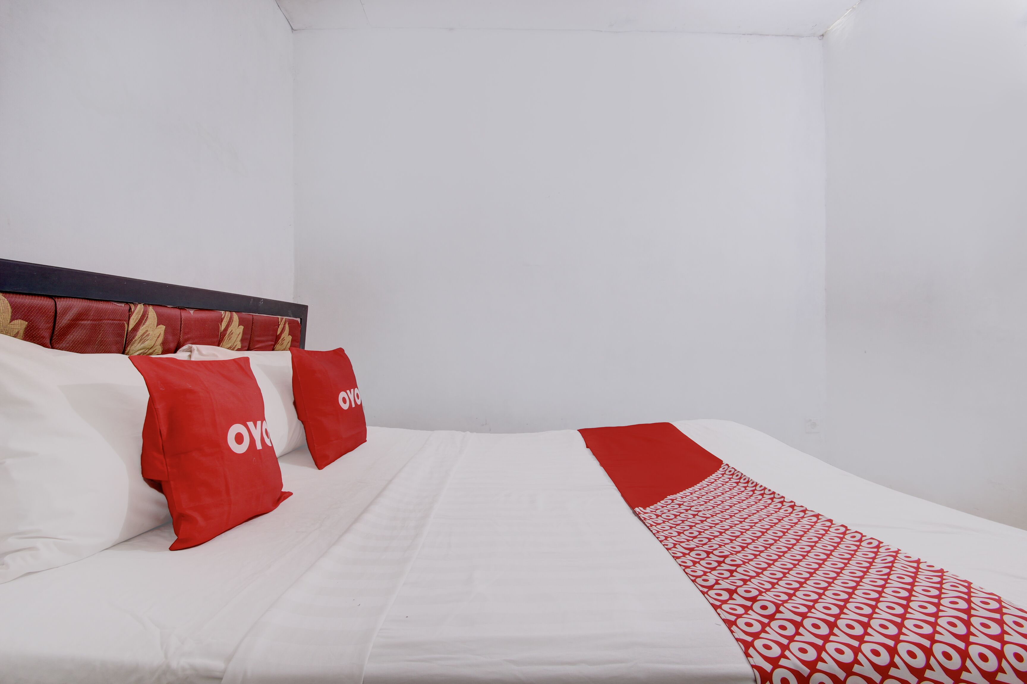 Habitación de hotel con cama, ropa de cama blanca y almohadas rojas con el texto "OVYO".