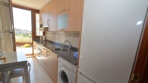 Eine Küche mit Waschmaschine, Spüle und Fenster mit Blick auf einen Balkon.