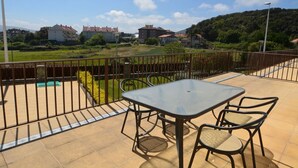 Ein Balkon mit Tisch und Stühlen, einem Metallzaun und Blick auf Häuser und Grünflächen im Hintergrund.