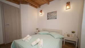 A bedroom with a bed, two bedside tables, a nightstand, a painting on the wall, and a door.