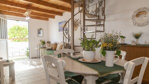 A dining area with a wooden ceiling, white chairs, a table with a green tablecloth, and potted plants.