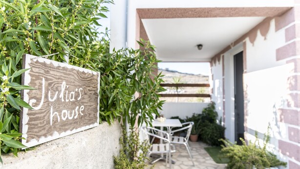 A wooden sign reading "Julia's house" in a garden setting with a patio and outdoor furniture.
