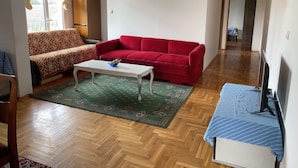 Un salon avec un canapé à motifs, un canapé rouge, une table basse blanche et un lit à rayures bleues.