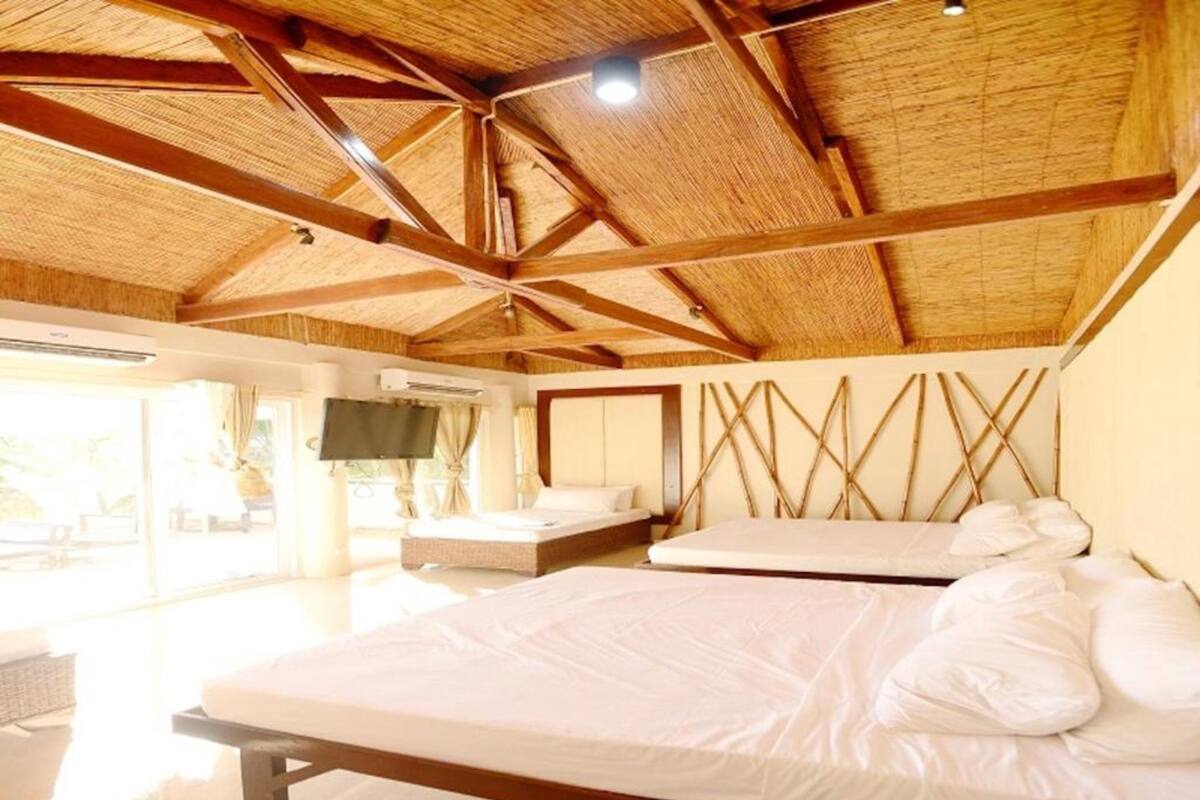 Una habitación amplia con techo de madera alto, dos camas, un televisor y un gran ventanal.