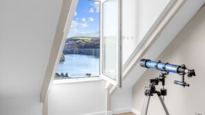 Een telescoop in een kamer met een groot raam met uitzicht op water en heuvels.