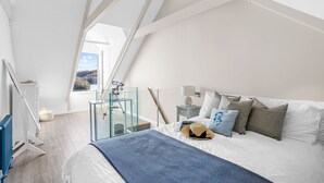 Een moderne slaapkamer met schuine plafonds, een glazen balkon, een bed met witte lakens en uitzicht op de omgeving.