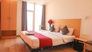 Una habitación de hotel con una cama, un armario de madera, una mesita pequeña y una mesita de noche.