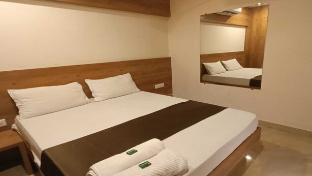 A hotel room with a large bed, a wooden headboard, a wall-mounted air conditioner, and a mirror. - Hotel Apple Inn (Mumbai)