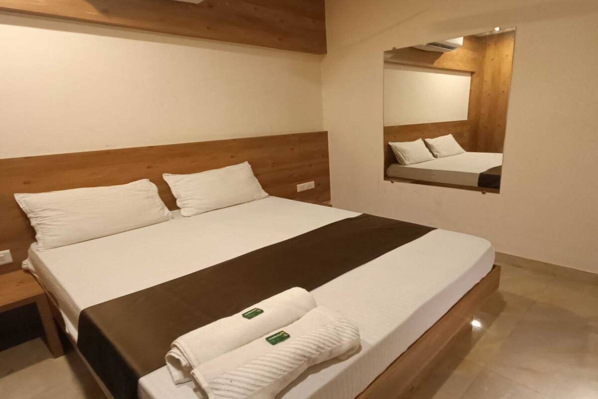 A hotel room with a large bed, a wooden headboard, a wall-mounted air conditioner, and a mirror.