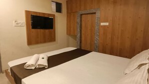 A hotel room with a wooden headboard, a bed with white bedding, a flat-screen TV mounted on the wall, and a small window. - Hotel Apple Inn (Mumbai)