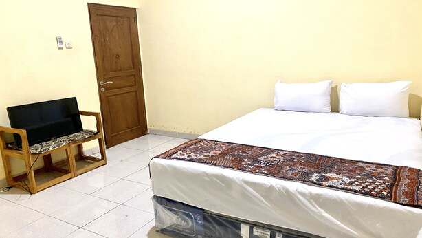 A bedroom with a bed, a wooden chair, a television, and a door. - Capital O 93601 Manda Homestay Syariah (Pleret)
