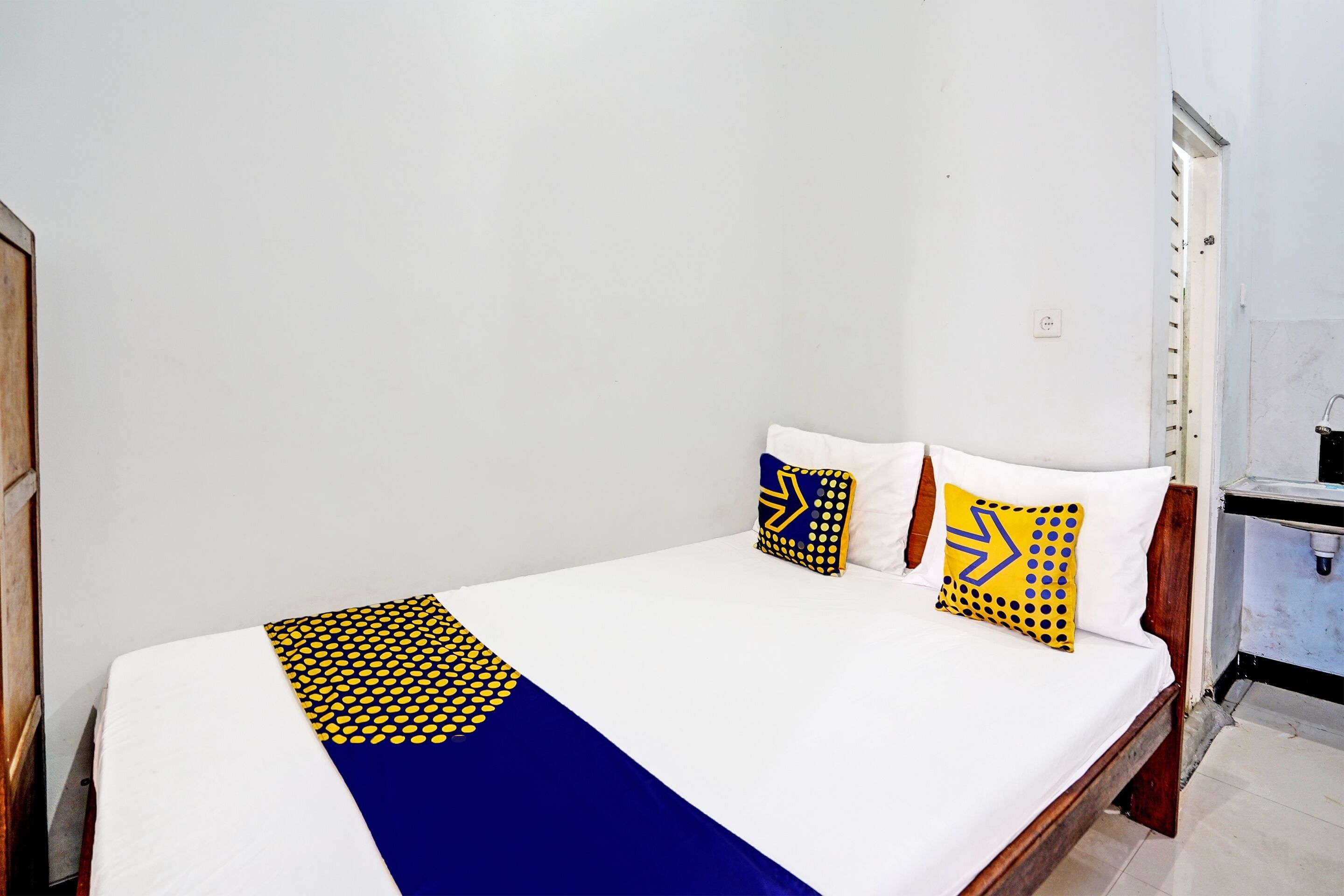 A single bed with a white mattress, a blue and yellow patterned bedspread, and two pillows with geometric designs.
