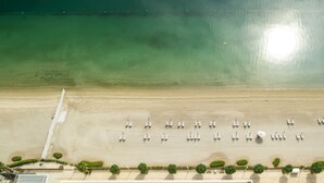 Luchtbeeld van een strand met rijen ligbedden en een helder uitzicht op de oceaan.