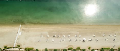 An aerial view of a beach with rows of sun loungers and a clear view of the ocean.