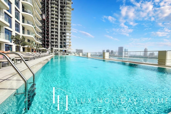 A poolside view of a high-rise building with a clear blue sky and distant cityscape.