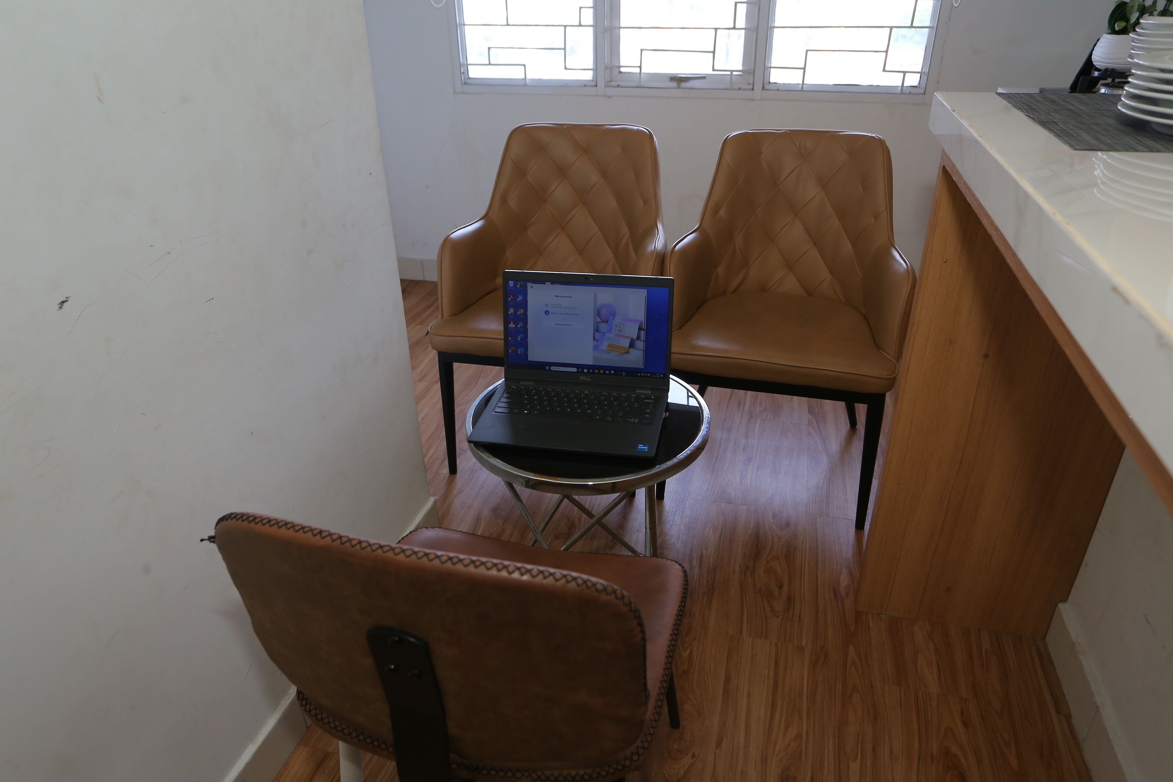 A small room with a laptop on a table, two leather chairs, and a window with blinds.