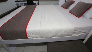 Ein ordentlich bezogenes Bett mit weißer und brauner Bettdecke und roter Zierleiste, eine grau gepolsterte Bank und ein weißer Kopfteil.