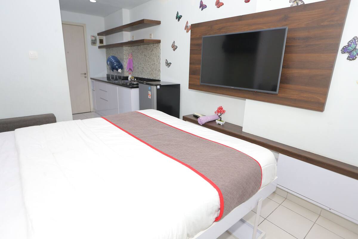 Ein Schlafzimmer mit einem Bett, einem an der Wand befestigten Fernseher, einer kleinen Küchenzeile und Schmetterlingsmotiven an der Wand.