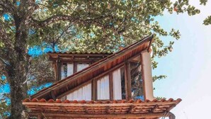 A rustic wooden building with a porch, a surfboard, and a mountainous backdrop. - Chalet Bromelias, Praia do Sono, Sea View (Paraty)