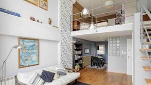 Un vaste espace de vie doté d’un haut plafond, une chambre en mezzanine accessible par un escalier, et un coin repas offrant une vue agréable.