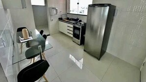 Una cocina moderna con un refrigerador de acero inoxidable, una estufa y un comedor con una mesa de vidrio y sillas.