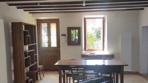 A room with a wooden bookshelf, a dining table with chairs, a window with a view of greenery, and a black leather couch. - Lac Aigueblette Maison de Charme (Nances)