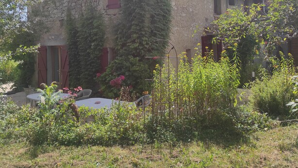 A stone house with a tiled roof, ivy-covered walls, and a garden with plants and flowers. - Lac Aigueblette Maison de Charme (Nances)