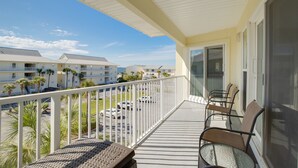 A balcony with a white railing, a glass door, and a seating area with chairs and a table. - Awesome condo with pool, across from beach access (Navarre)