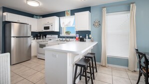 A kitchen with white cabinets, a stainless steel refrigerator, a microwave, an oven, and a sink. There is a window with blinds and a curtain. - Awesome condo with pool, across from beach access (Navarre)
