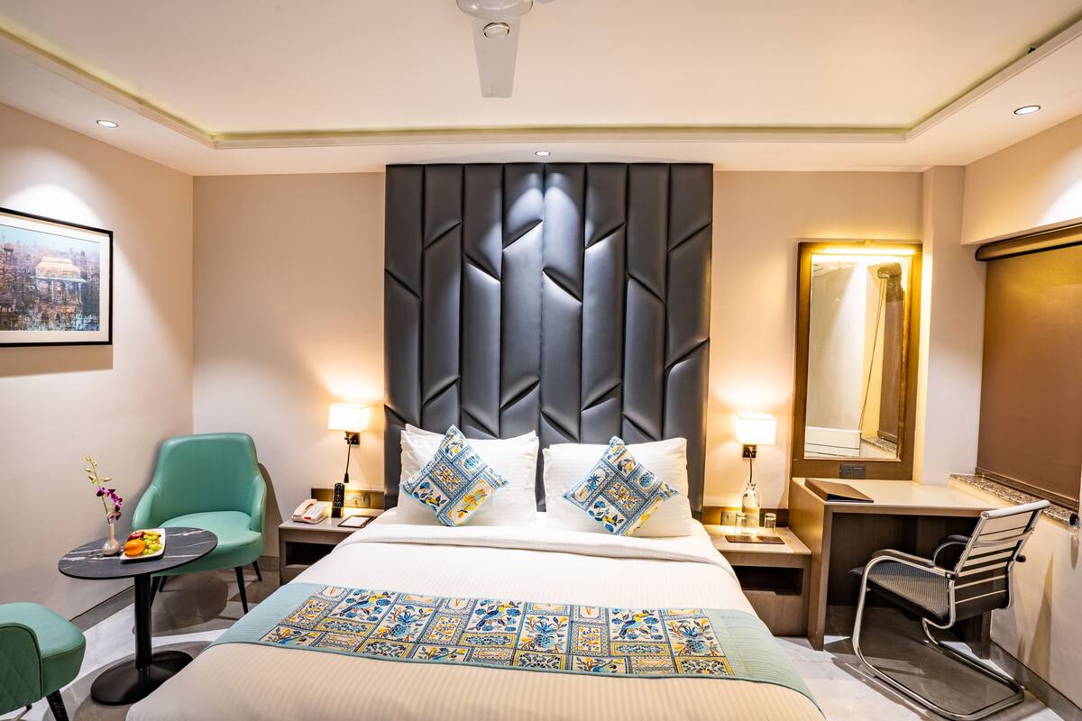 A hotel room with a large bed, a desk, a chair, and a mirror.