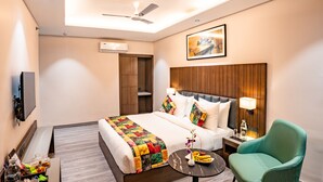 Une chambre d’hôtel avec un lit, un bureau, une chaise, un ventilateur de plafond et un tableau au mur.