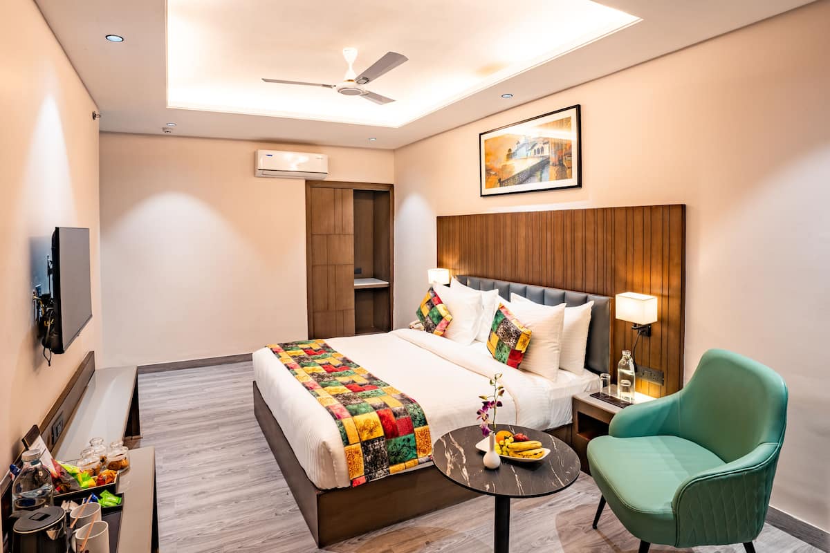 A hotel room with a bed, a desk, a chair, a ceiling fan, and a painting on the wall.