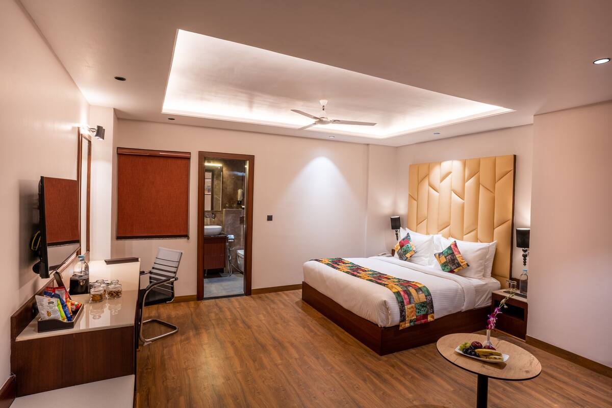A modern hotel room with a large bed, a desk with a chair, a vanity, and a ceiling fan.