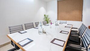 Une salle de conférence avec une table en marbre blanc, des chaises noires et grises, une plante en pot et une fenêtre avec un store marron.